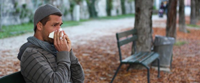 Man on park bench with cold blowing nose